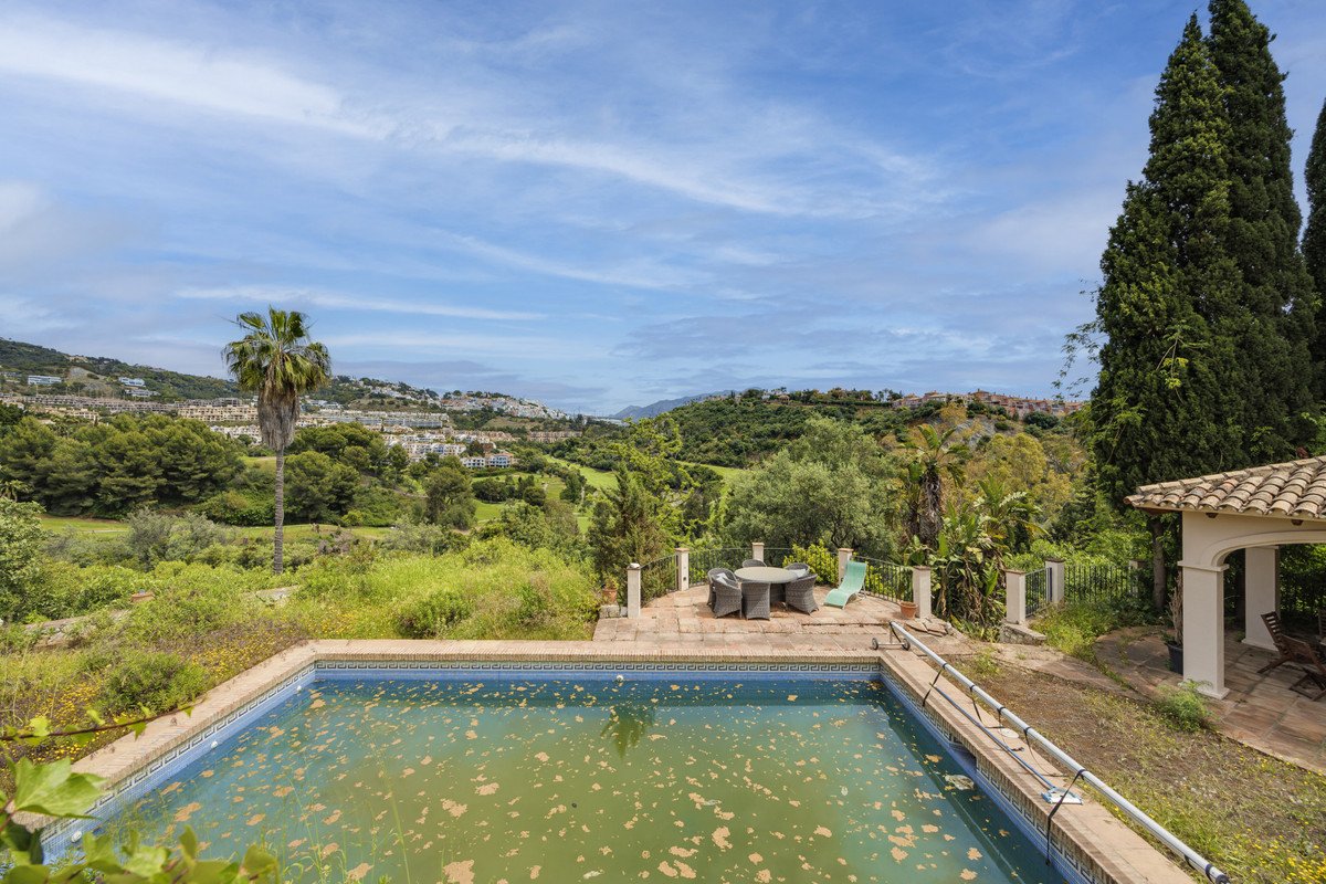 Villa with pool overlooking lush green hills and distant town under blue sky.