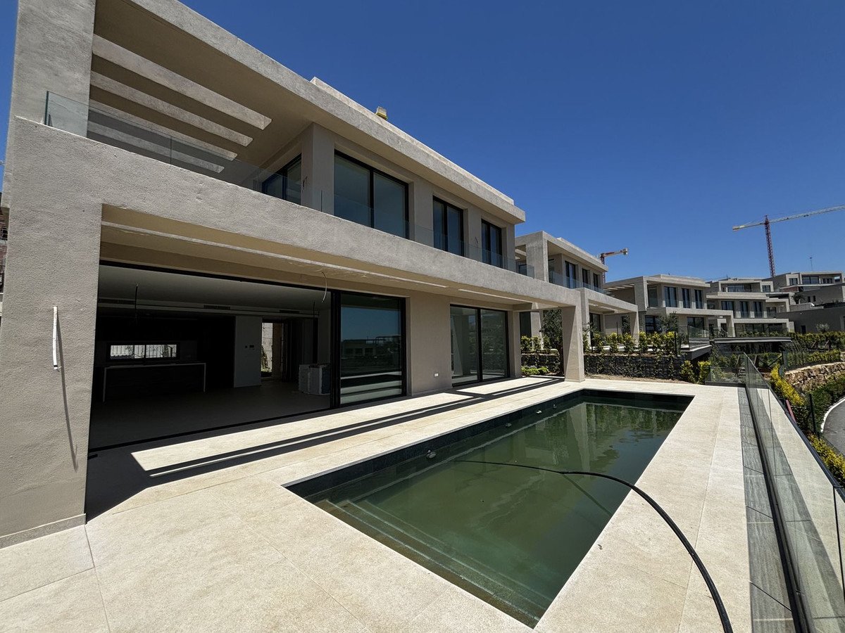 Modern villa with pool, glass walls, and outdoor terrace under clear blue sky.