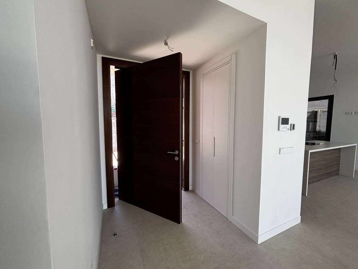 Modern hallway with dark wooden door, white walls, and tiled floor, leading to kitchen area.