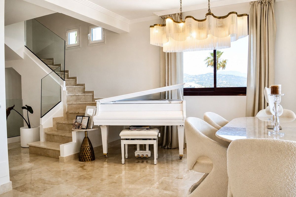 Elegant living space with white grand piano, marble stairs, and ocean view through large window.