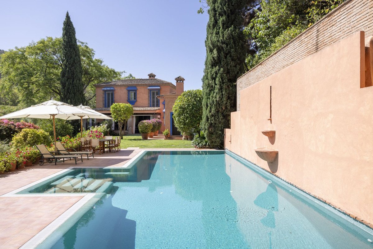 Luxurious villa with private pool, sun loungers, and lush garden under clear blue sky.