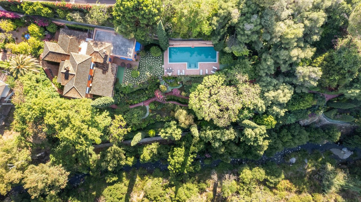 Aerial view of a villa with a pool, surrounded by lush greenery and trees.