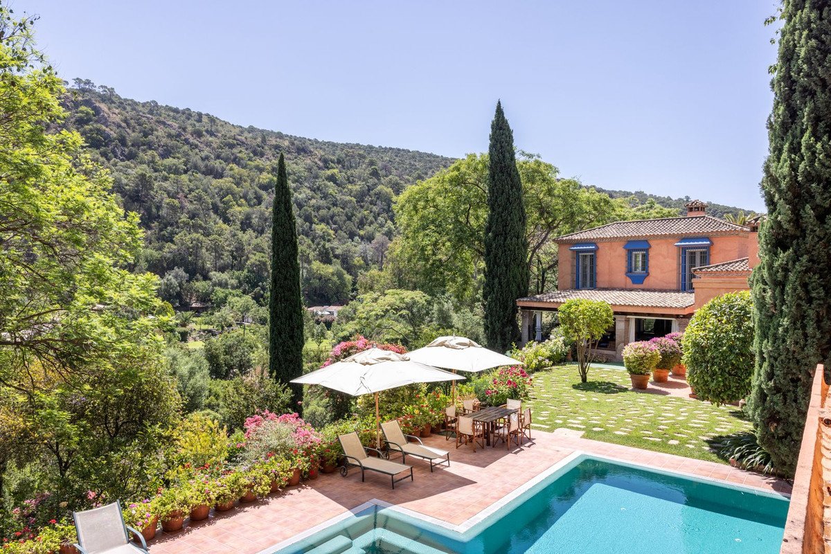 Villa with pool, garden, and mountain views under clear blue sky.