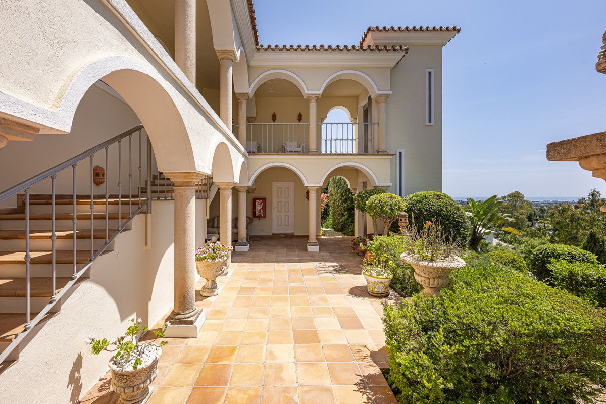 A sunlit courtyard with arched walkways, tiled floors, and lush greenery overlooking a scenic landscape.
