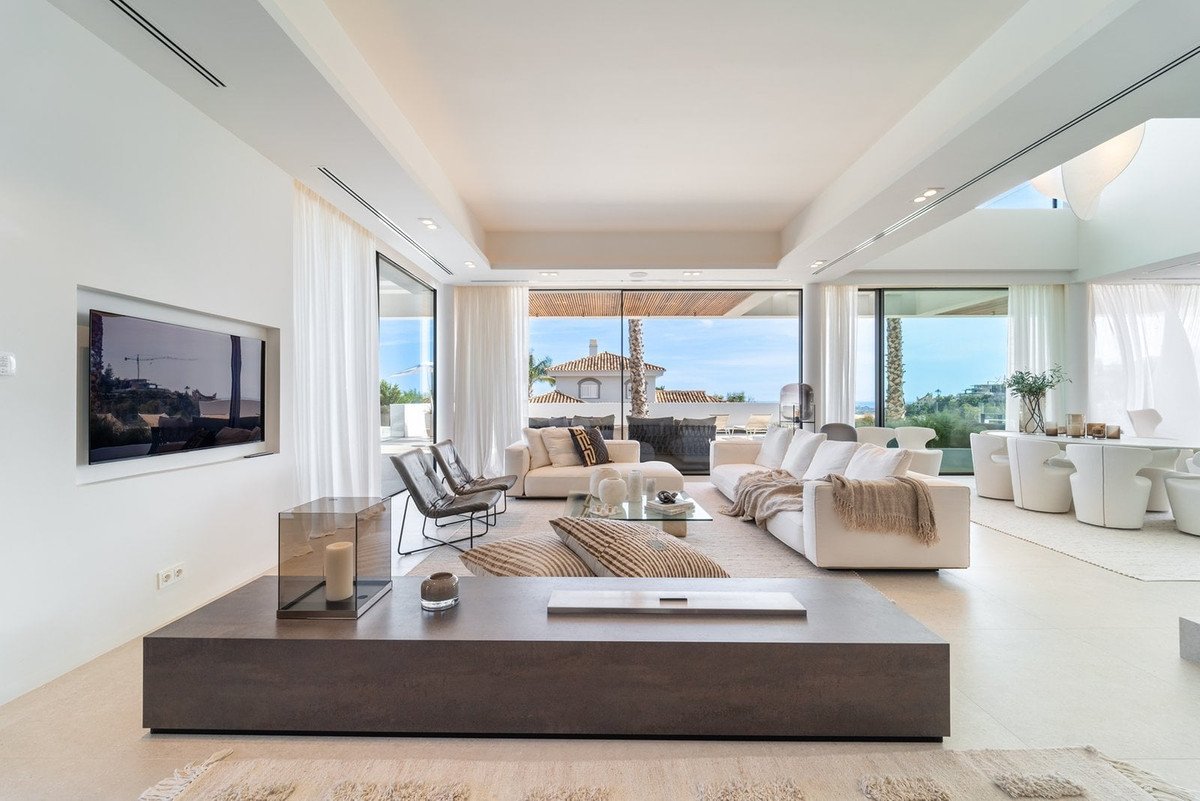 Modern living room with large windows overlooking the sea and palm trees.
