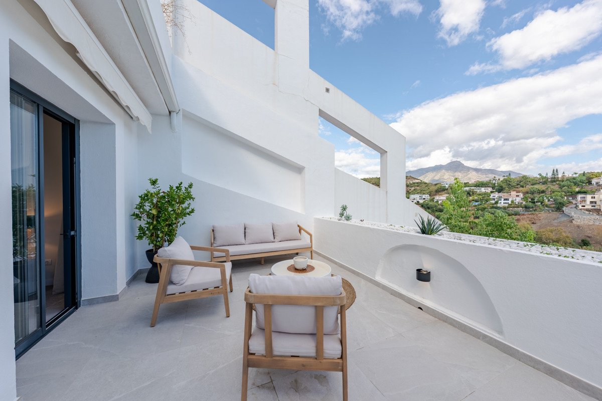 Modern terrace with seating area, offering a scenic view of rolling hills and mountains under a blue sky.