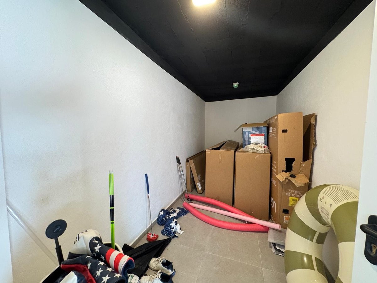 Storage room with boxes, golf clubs, pool noodles, and an inflatable ring. Black ceiling and white walls.