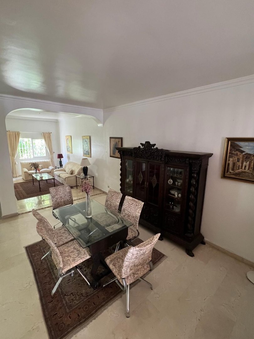 A dining room featuring a glass-top table with six chairs and a large antique display cabinet.