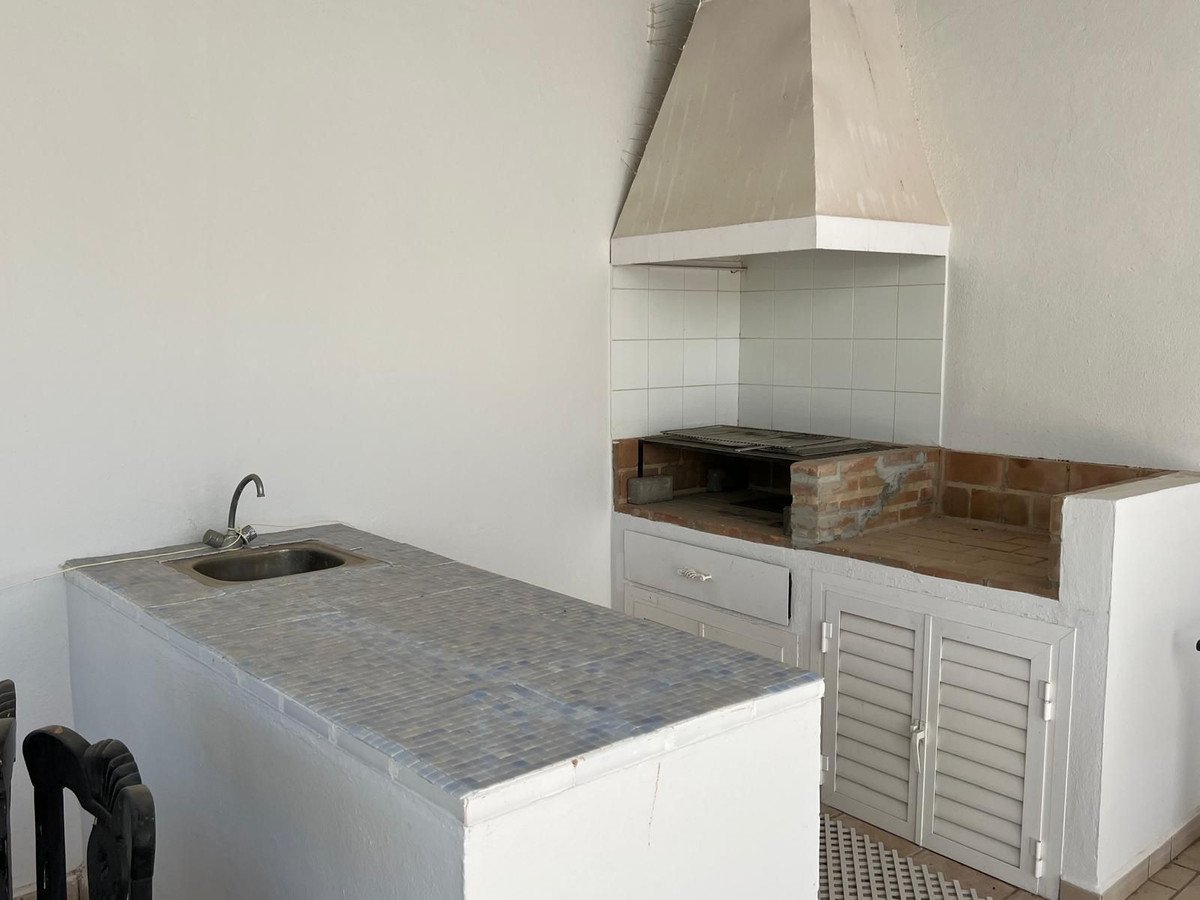 Outdoor kitchen area with a built-in brick grill, a sink, and counter space.
