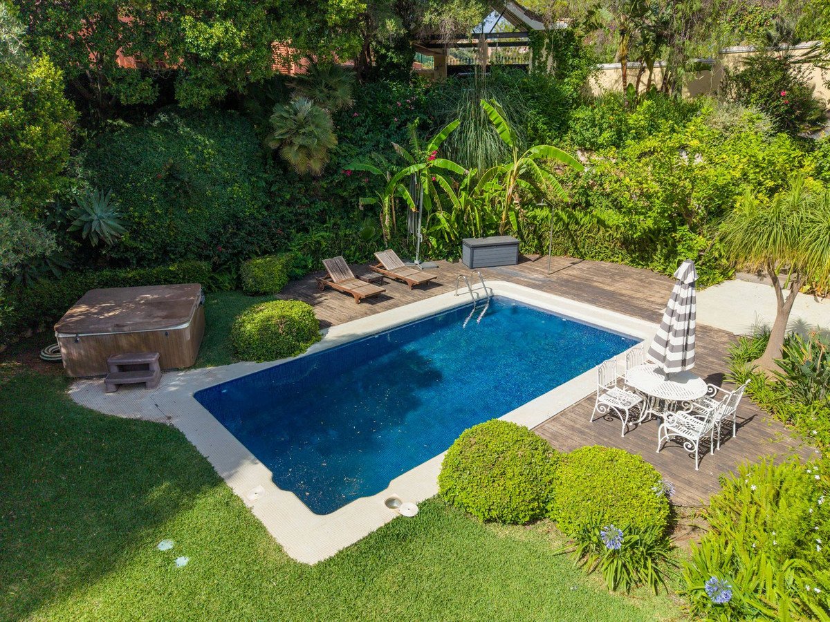 A luxurious backyard with a sparkling swimming pool, a hot tub, wooden deck, and lush green landscaping.