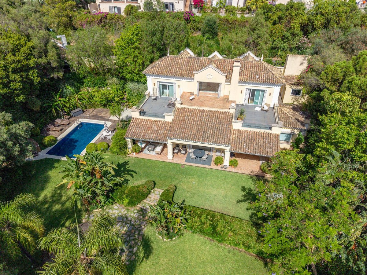 Aerial view of a luxury villa with a swimming pool, lush green gardens, and outdoor seating areas.