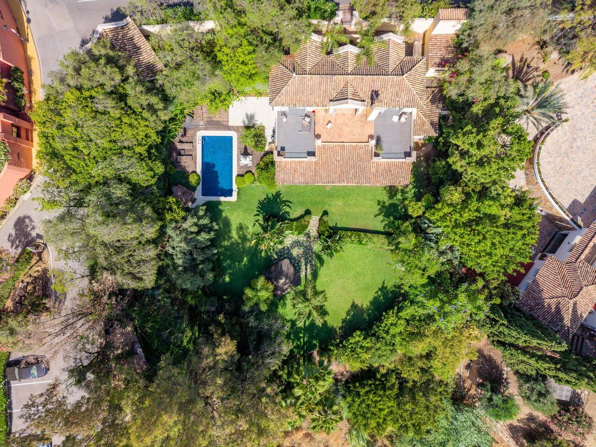 Aerial view of a luxurious villa with a swimming pool, lush green garden, and mature trees surrounding the property.
