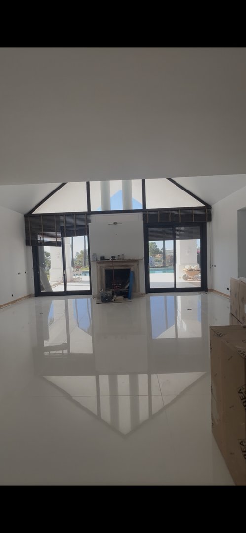 Spacious modern living room with a fireplace, high vaulted ceiling, and large glass doors opening to a pool area.