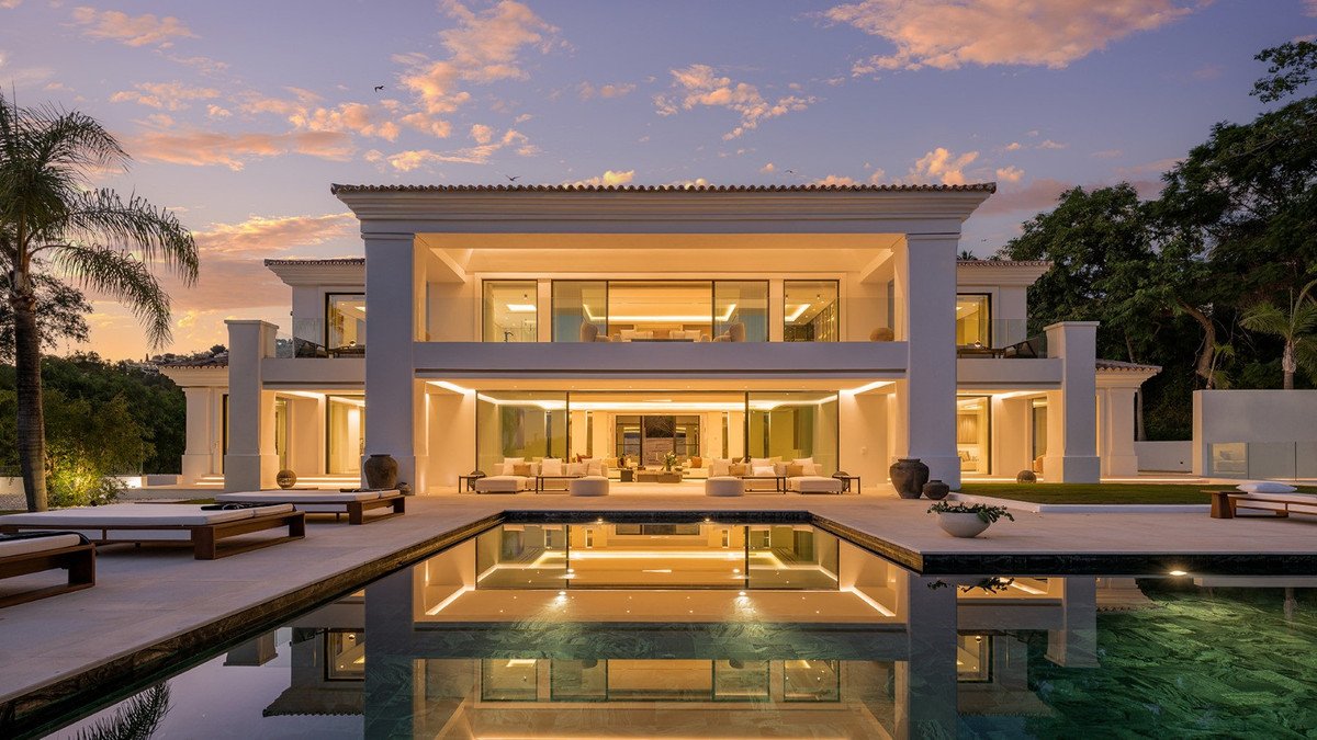 Luxurious modern villa at sunset with a swimming pool, lounge chairs, and extensive outdoor living spaces.