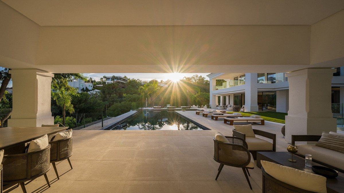 Modern villa with infinity pool, sun loungers, and outdoor seating area with a beautiful sunset view.