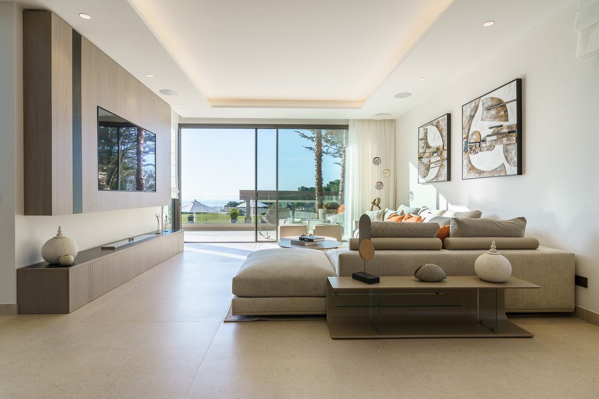 Modern living room with large sofa, coffee table, and sea view through sliding glass doors.