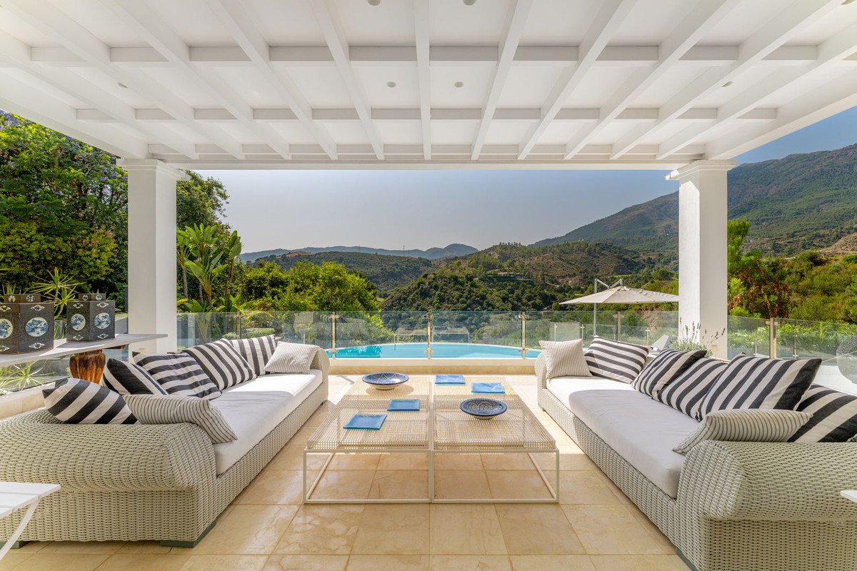 Outdoor covered patio with seating, a swimming pool, and a stunning view of green mountains under a clear sky.