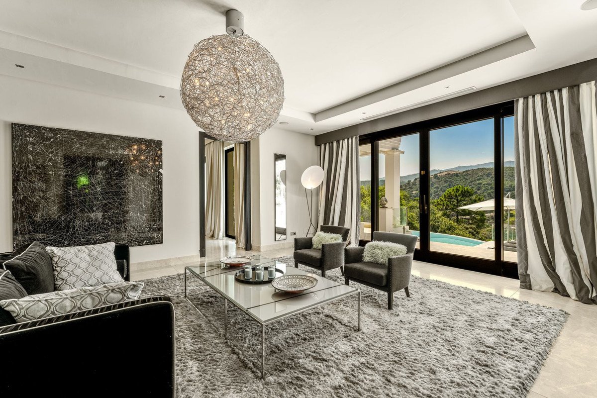 Modern living room with plush rug, stylish furniture, and panoramic views of a pool and mountains through large glass doors.