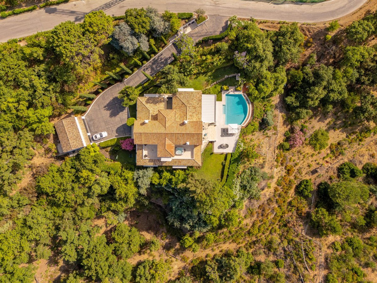 Aerial view of a large villa with a swimming pool, surrounded by trees and greenery, featuring a driveway and parking area.