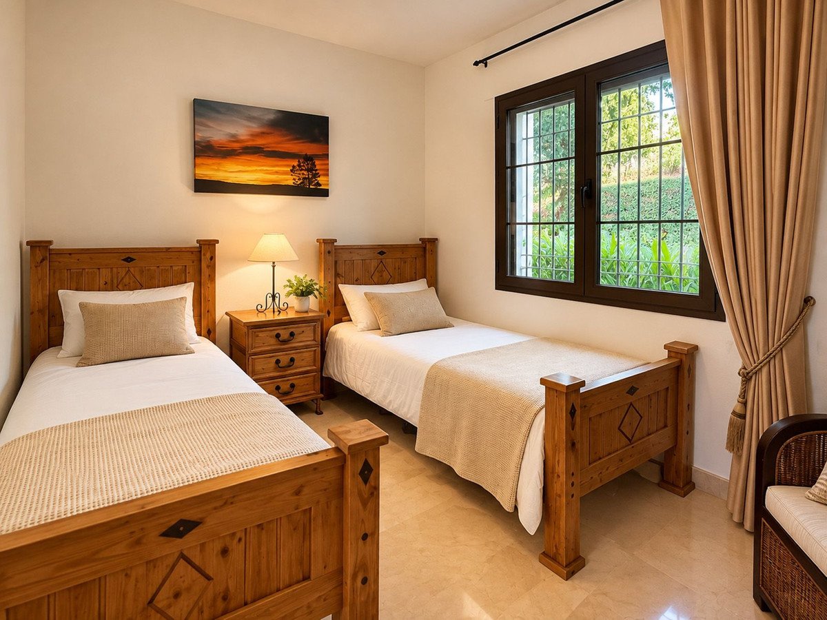 A cozy twin bedroom with wooden furniture, a bedside lamp, and a serene sunset landscape painting above the bed.