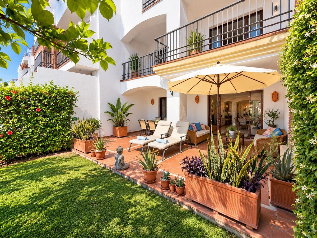 Terrace with sun loungers, seating area under umbrella, and a lush garden with plants and lawn area.