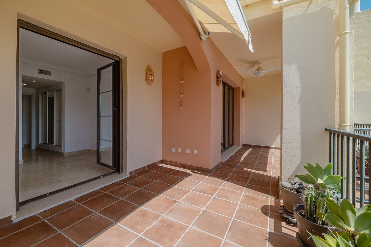 A spacious tiled terrace with glass doors opening inside, featuring potted plants and a retractable awning.