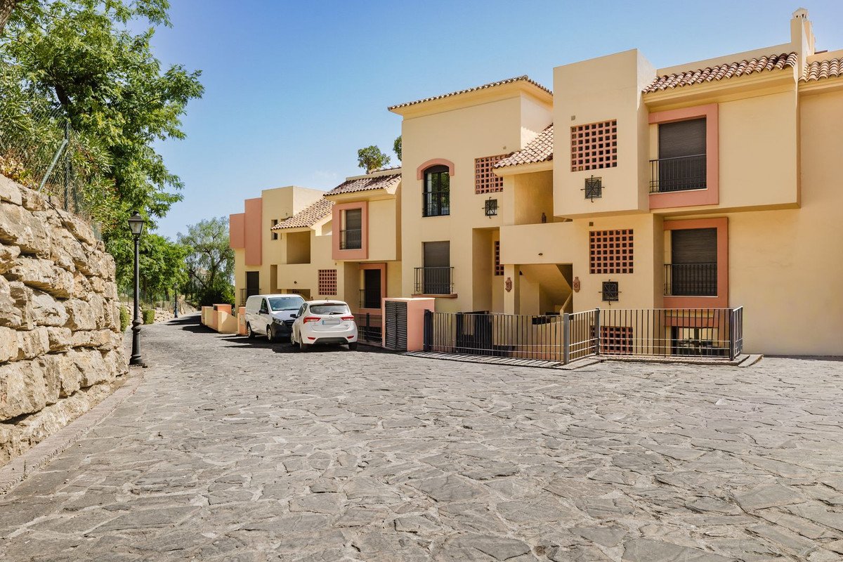 Exterior view of modern terrace houses with balconies and parked cars in front on a sunny day.