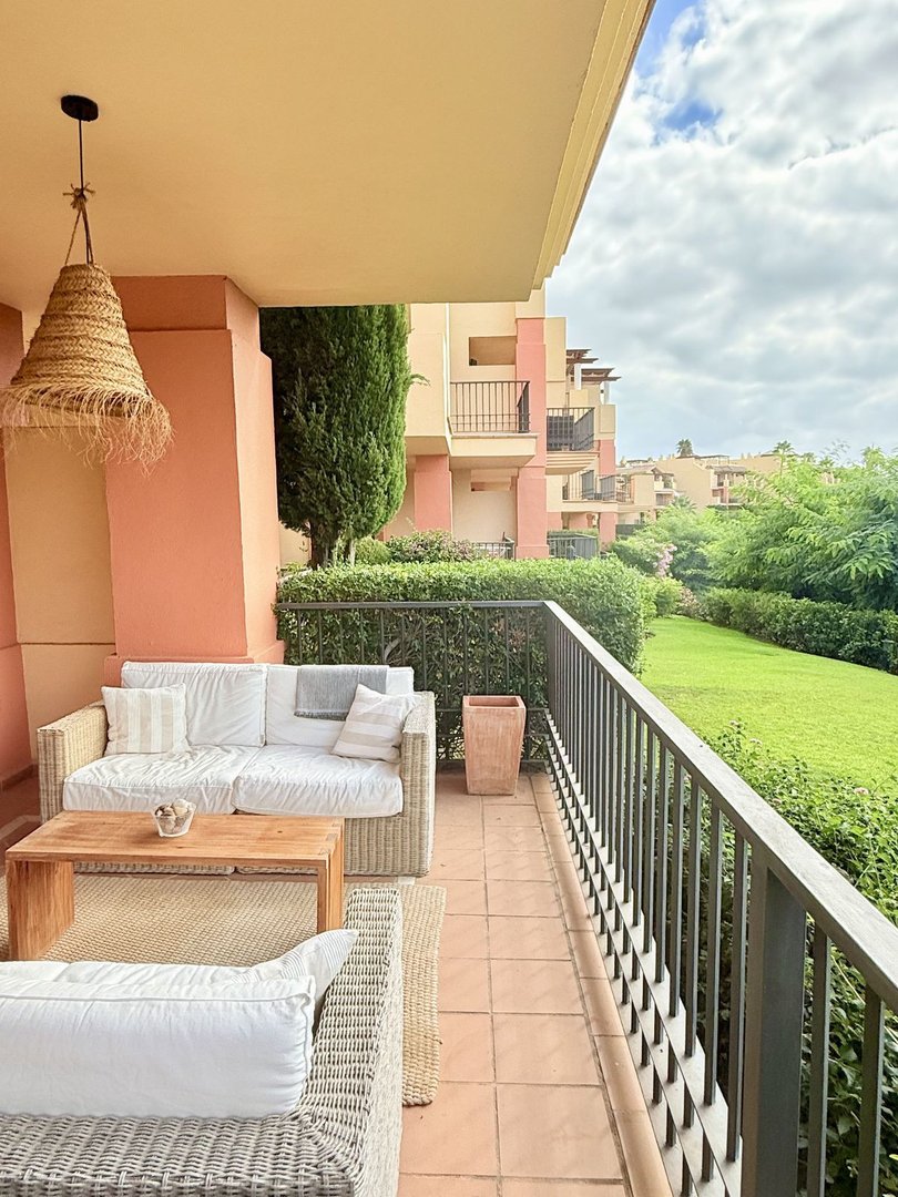 Comfortable outdoor seating area on a terrace with a view of a lush green garden and apartments.