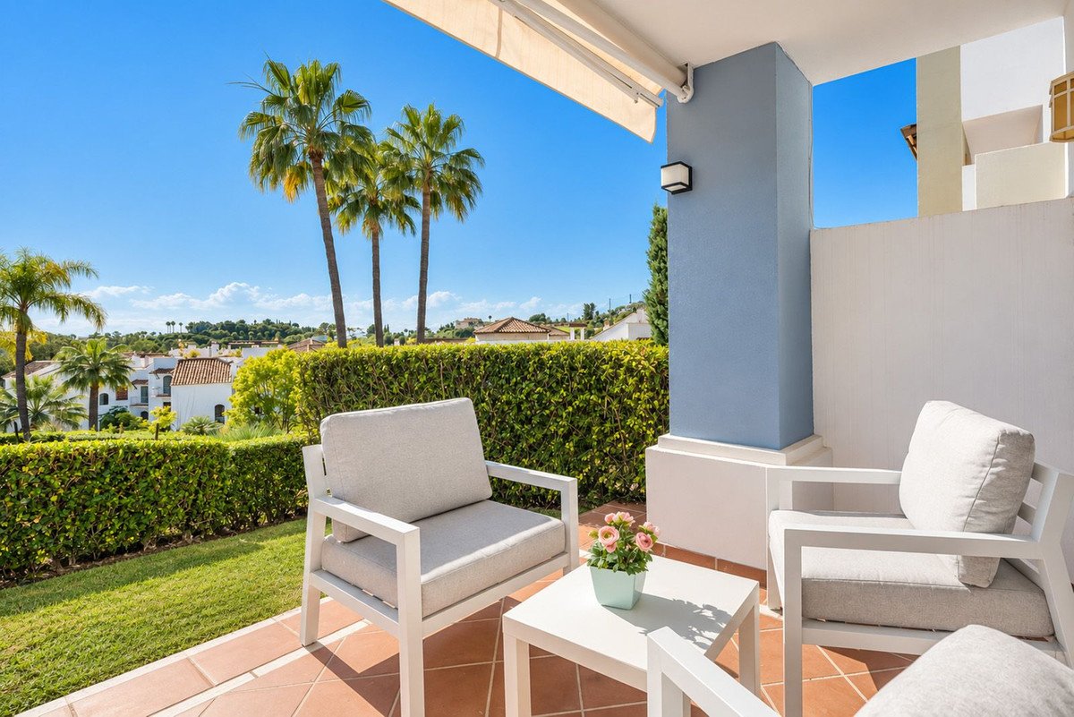 Terrace with comfortable seating area, overlooking lush greenery, palm trees, and houses under a clear blue sky.