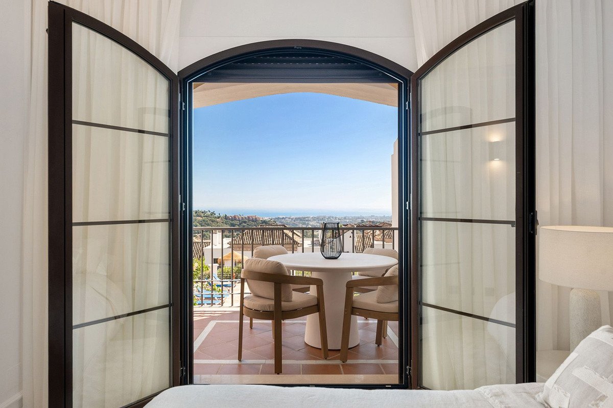 Bedroom with open doors to a balcony overlooking the ocean and city.