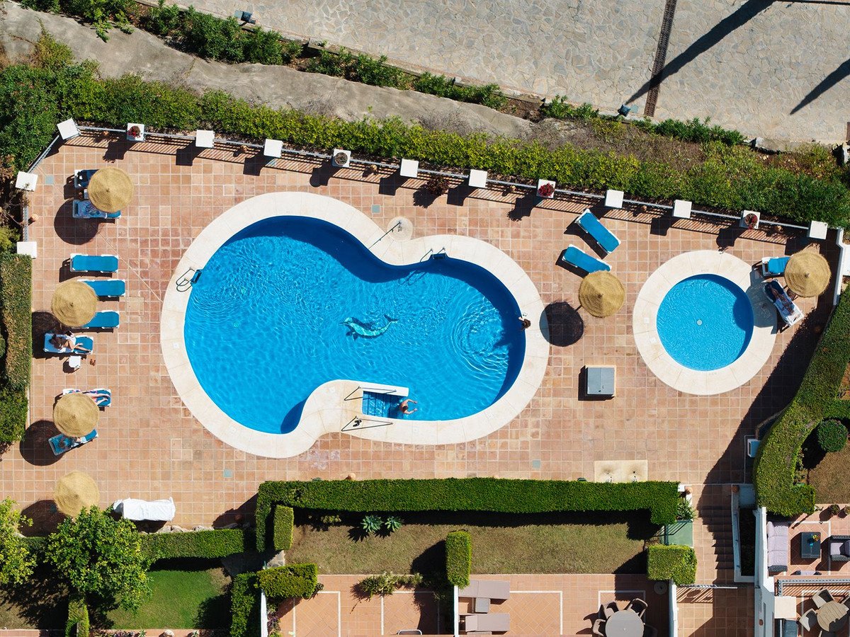 Aerial view of a large swimming pool with a smaller spa, surrounded by lounge chairs and umbrellas.