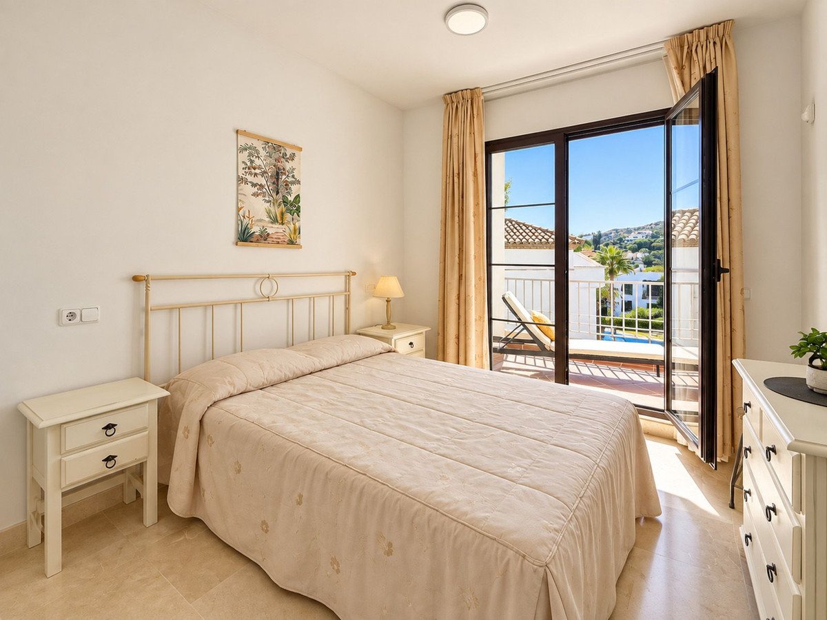 Bedroom with a queen bed, bedside tables, and a balcony door opening to a view of a pool and hills.