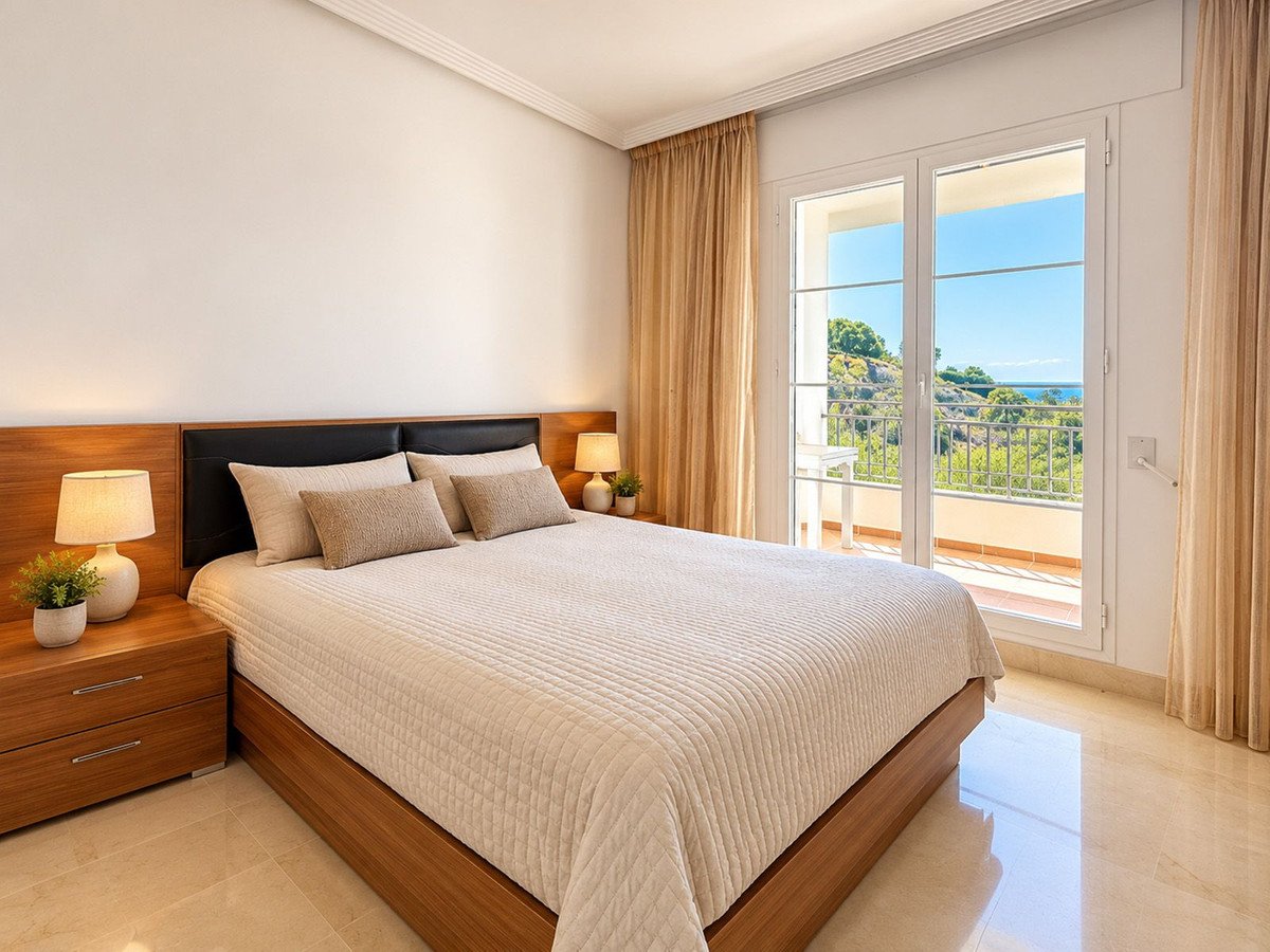 Bedroom with a large bed, nightstands, and double doors opening to a balcony with a sea and green landscape view.