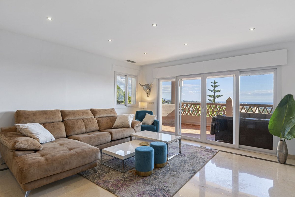 Spacious living room with sectional sofa, ocean view from balcony with ornate railings and palm tree accents.