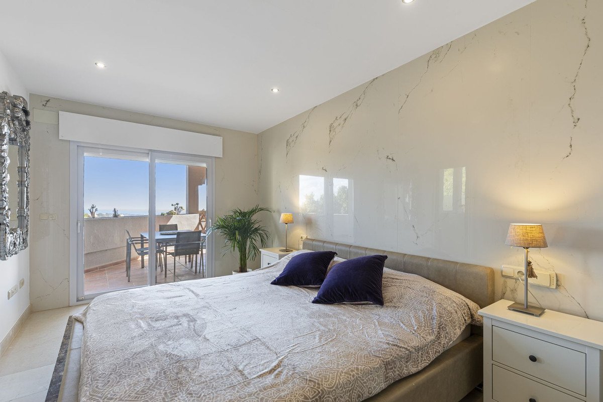 Bedroom with king-size bed, marble accent wall, and sliding doors leading to a balcony with a table and chairs overlooking the sea.