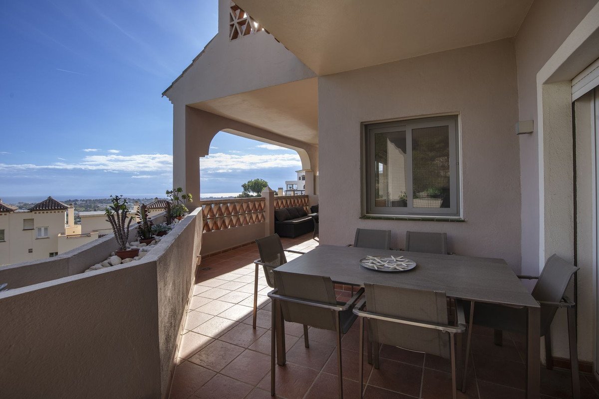 A covered terrace with a dining table and chairs, offering a sea view and overlooking buildings.