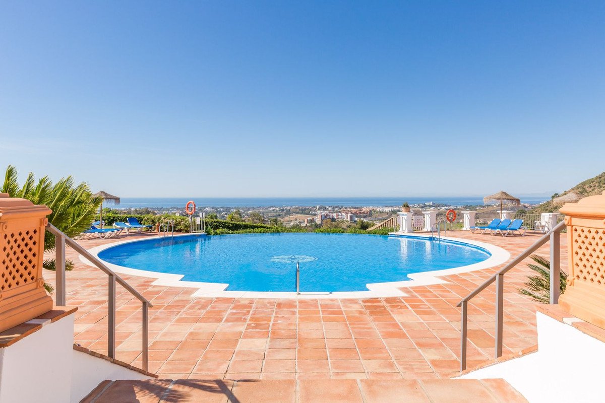 A large blue swimming pool with loungers and umbrellas, overlooking a coastal town and the sea.