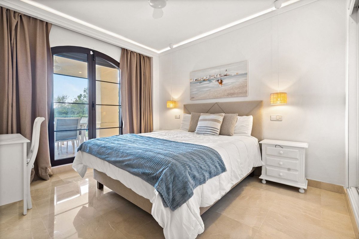 A cozy bedroom featuring a large bed, blue throw blanket, and a balcony with outdoor seating visible through glass doors.