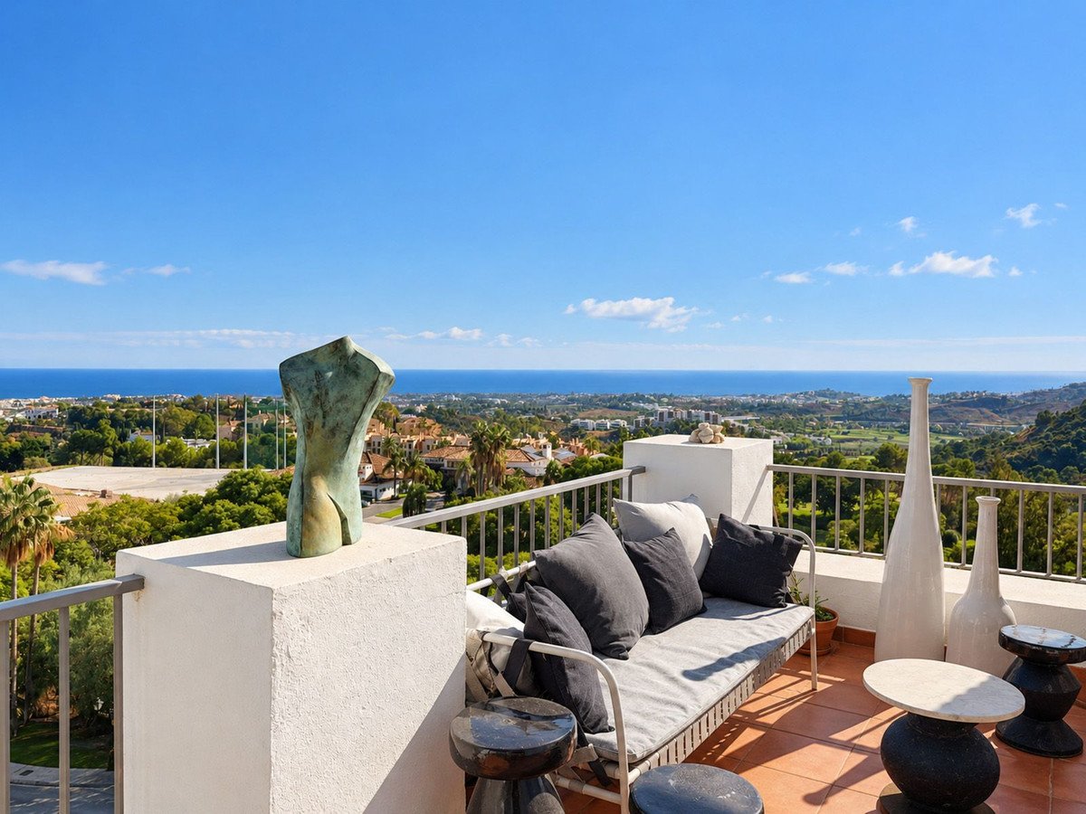 A terrace with sea view, featuring modern seating, decorative vases, and an abstract sculpture on a sunny day.