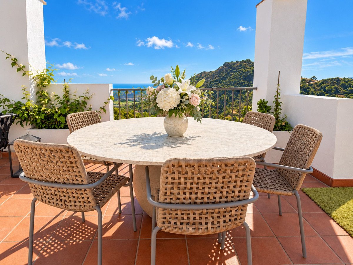 Outdoor dining set on a terrace with a beautiful sea and mountain view, decorated with a floral centerpiece.