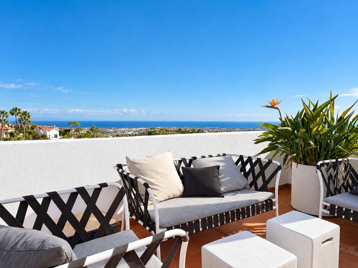 A modern outdoor seating area on a terrace with a stunning sea view and lush greenery.