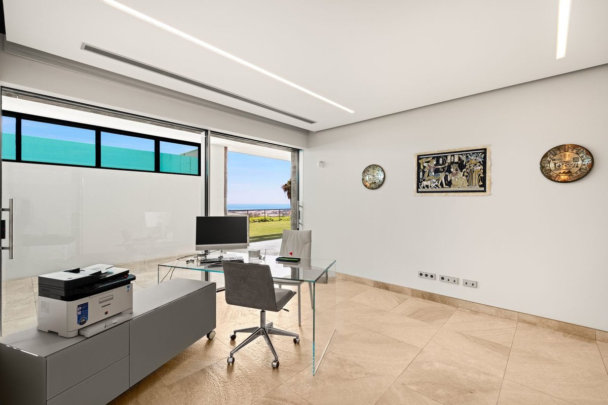 Modern office with a glass desk, computer, printer, and a stunning sea view through large sliding doors.