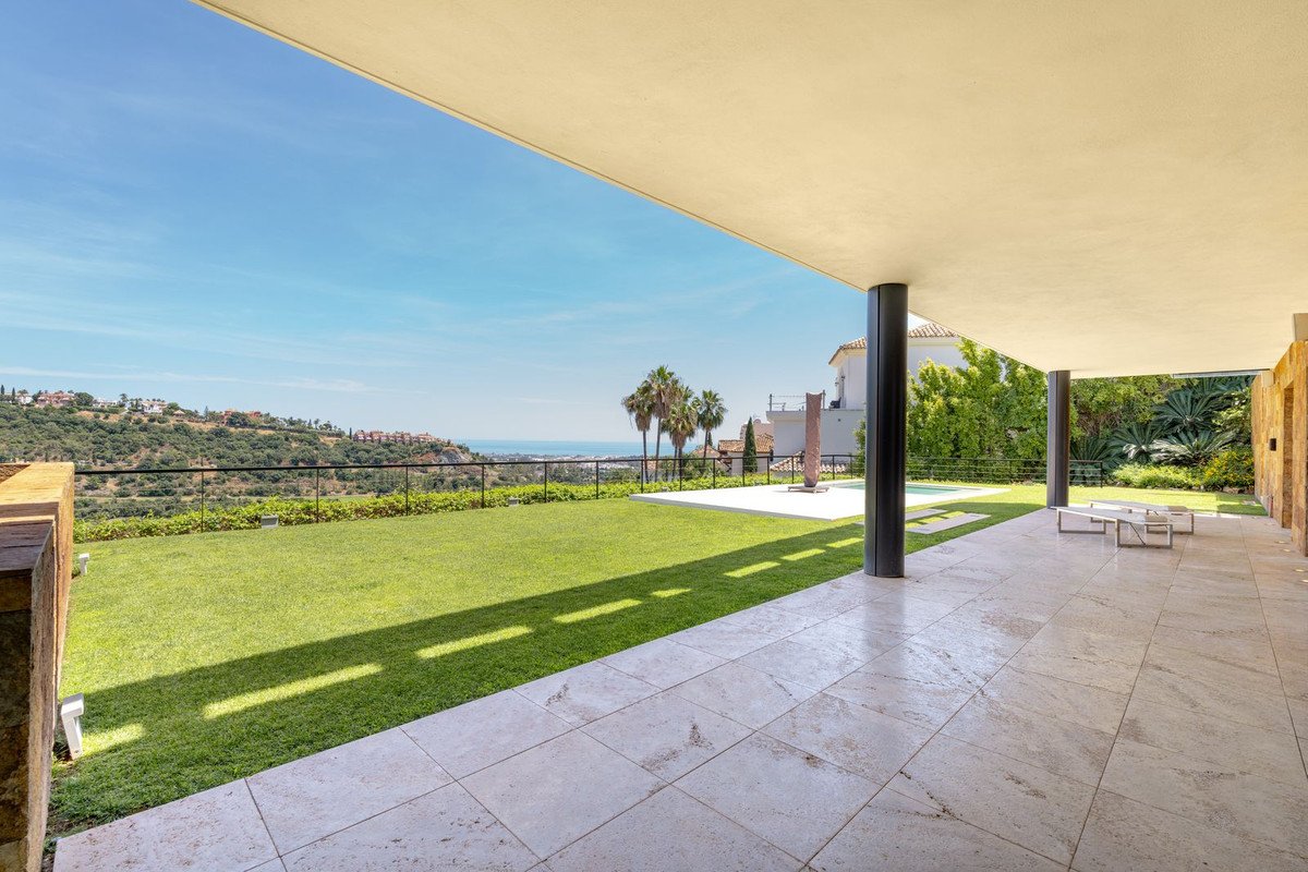 Spacious patio with sea view, overlooking a lush green lawn and distant hills under a clear blue sky.