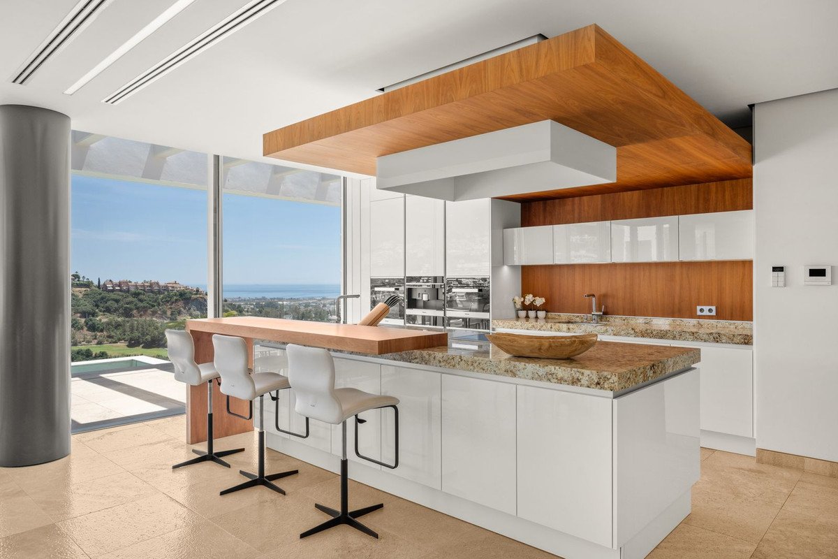 Modern kitchen with white cabinets, a wooden island and bar stools, overlooking a scenic sea view.