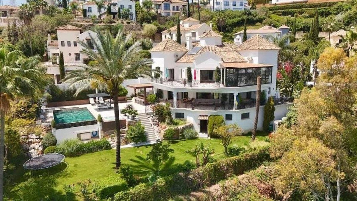 Spacious villa with a swimming pool, lush garden, trampoline, and multiple balconies, surrounded by greenery on a hillside.