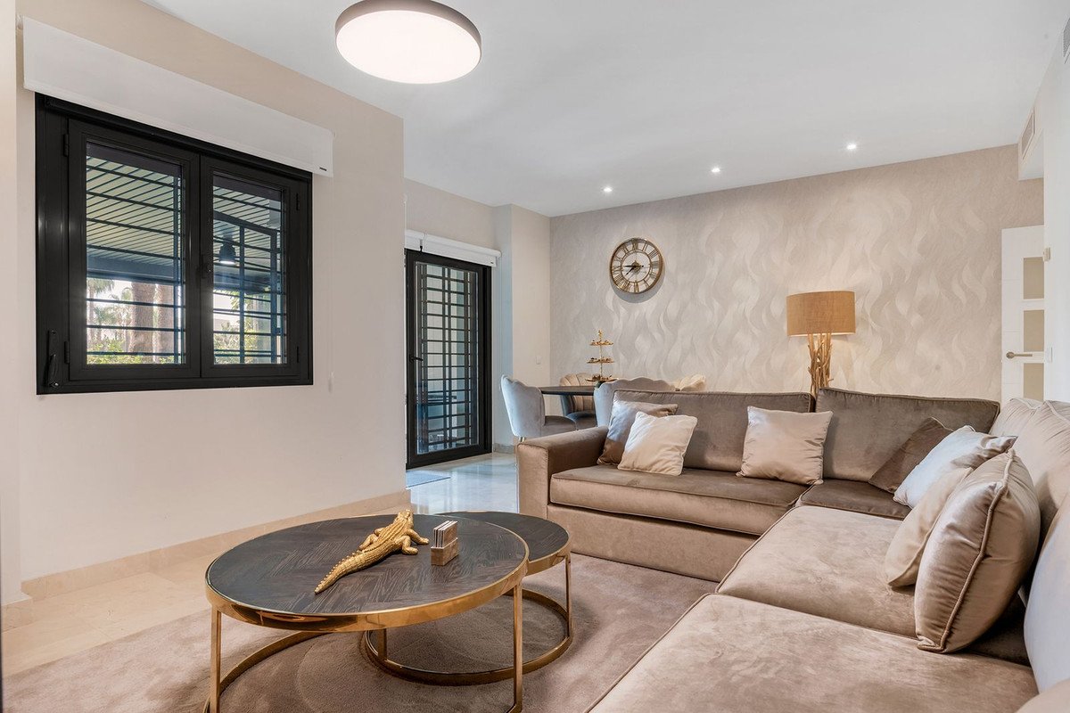 A spacious living room features a large sectional sofa, decorative coffee table, a wall clock, and a view of trees through the window.