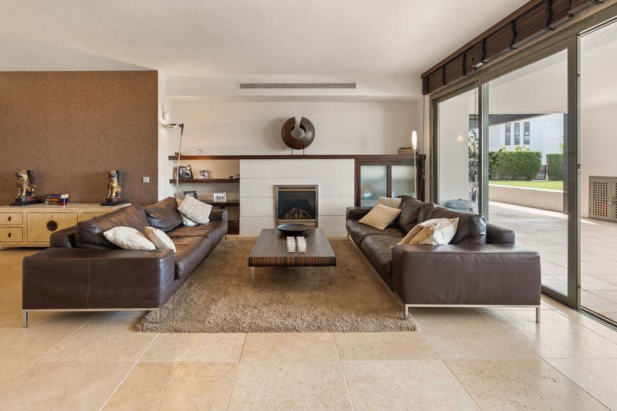 Modern living room with brown leather sofas, a fireplace, and large glass doors opening to an outdoor patio.