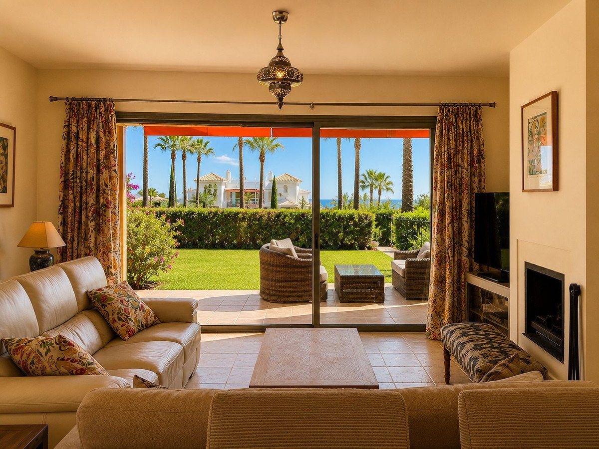 Living room with a large sofa, fireplace, and sliding doors opening to a garden with palm trees and a sea view.