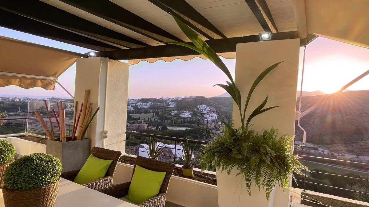 Terrace seating with bright green cushions offers a beautiful sunset view over a hillside town and distant mountains.