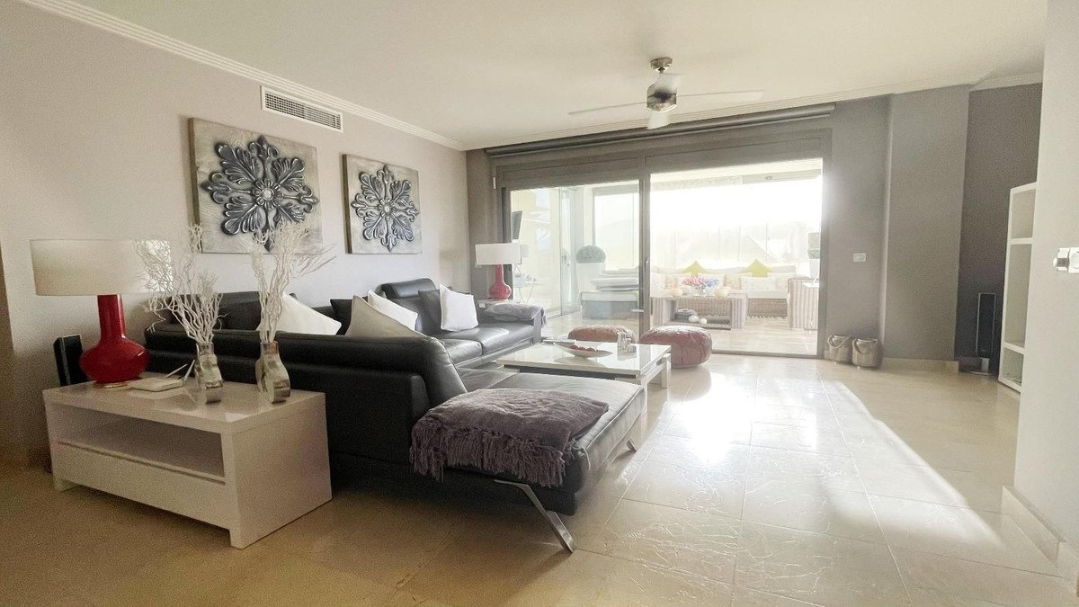 Modern living room with black leather sofa, white coffee table, and sliding doors leading to a patio with outdoor seating.